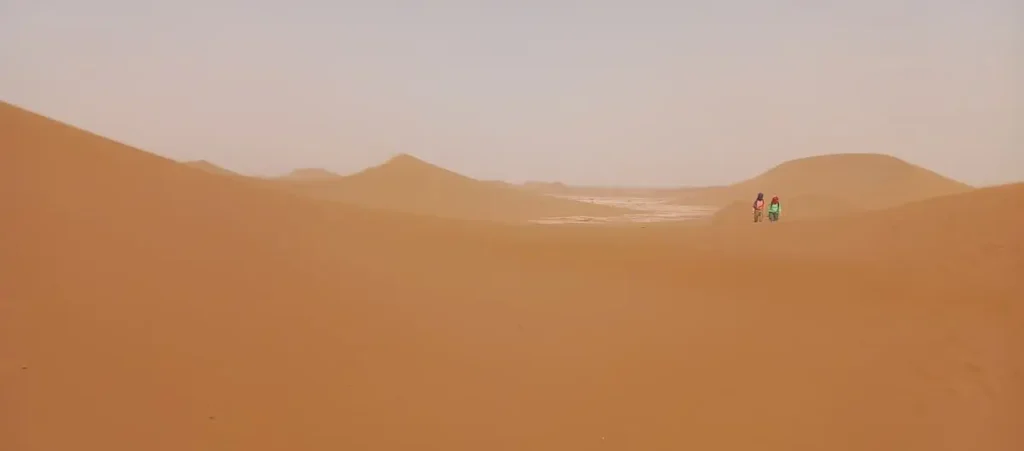Two hikers walking toward the Singing Dune near M’Hamid El Ghizlane in the Moroccan Sahara