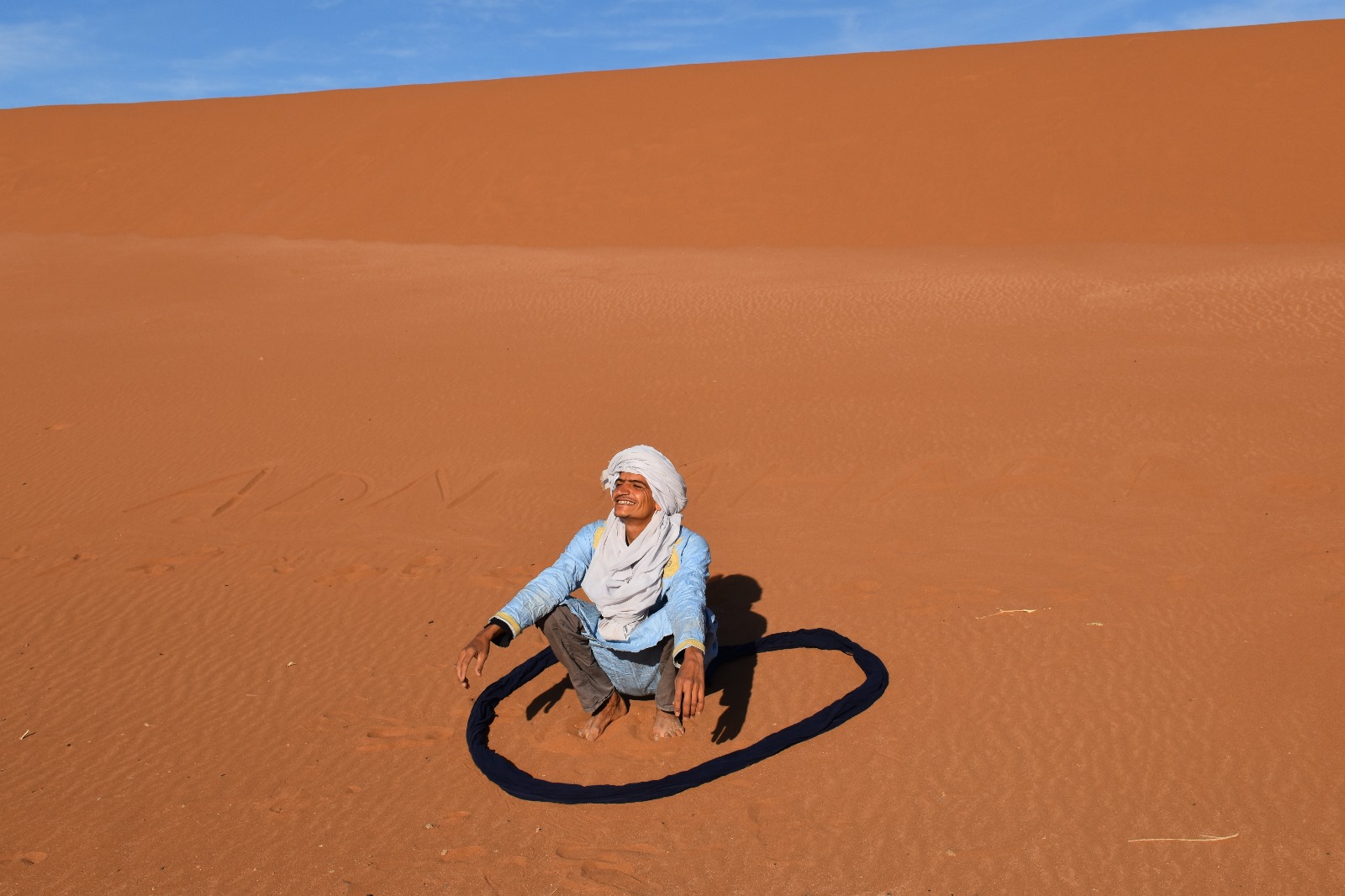 Lahsan, Sahara desert guide, sitting inside a heart drawn in the sand at sunset