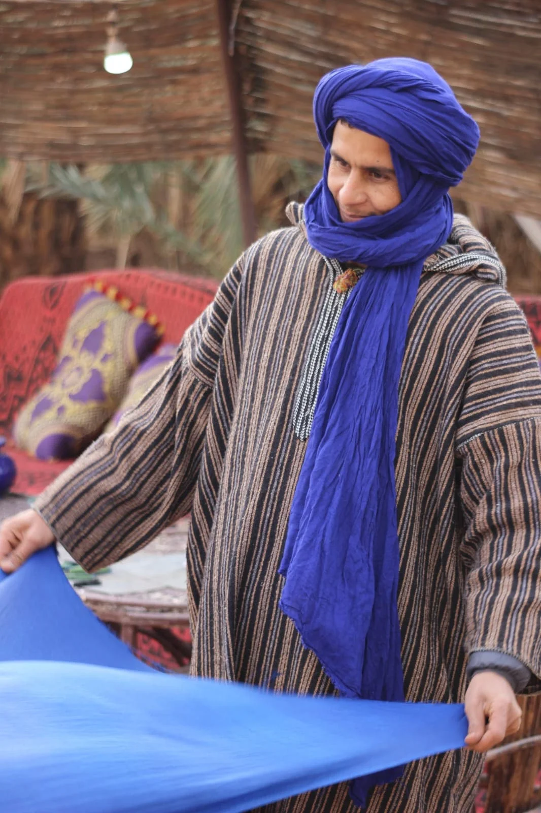 Nomadic camel driver Ahmed wearing traditional gray striped djellaba and blue cheche turban in the deserttraditional djellaba robe and cheche turban in the desert