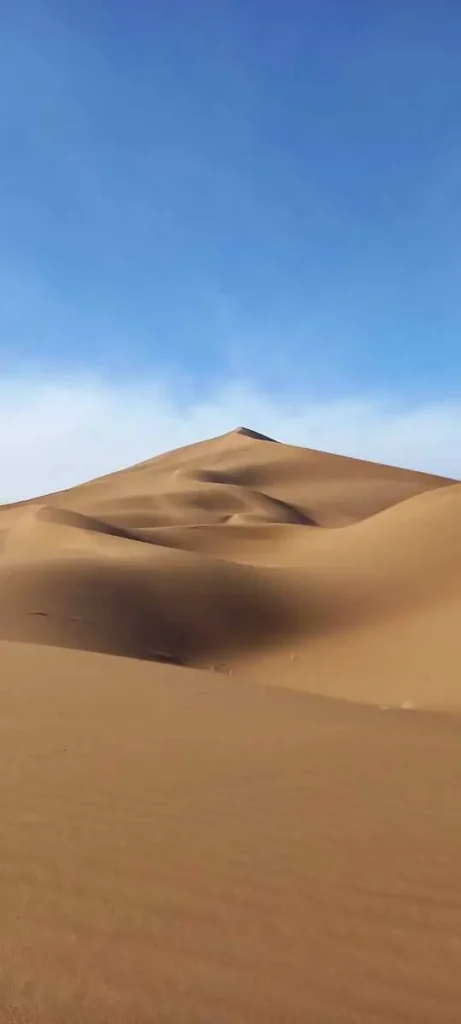 Dune paisible de Chegaga sous un ciel bleu parsemé de quelques nuages.