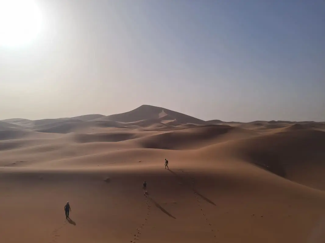 Three hikers heading toward the Singing Dune at sunset — authentic Sahara trekking experience from M'hamid Morocco
