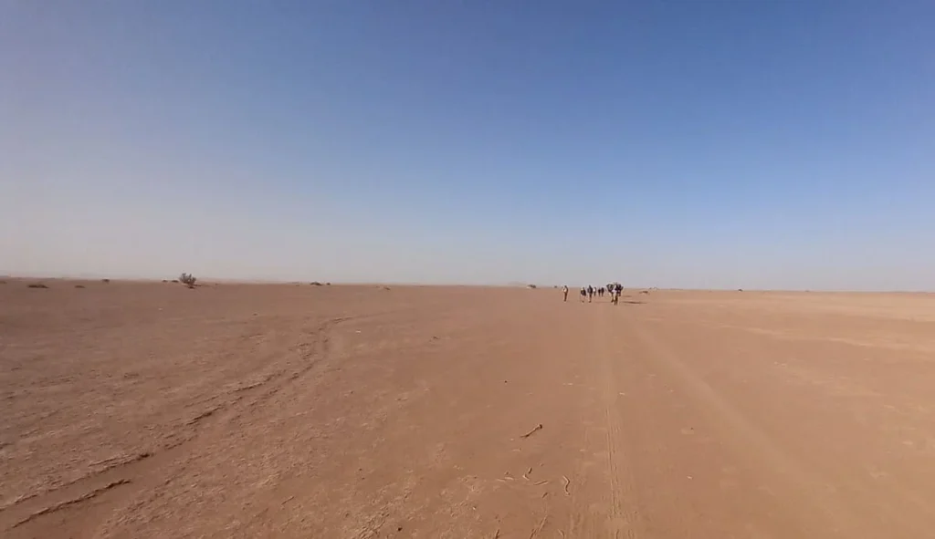 Group of trekkers heading to Erg Chigaga during a 6-day trek in the Moroccan desert, walking over sand dunes under a blue sky.