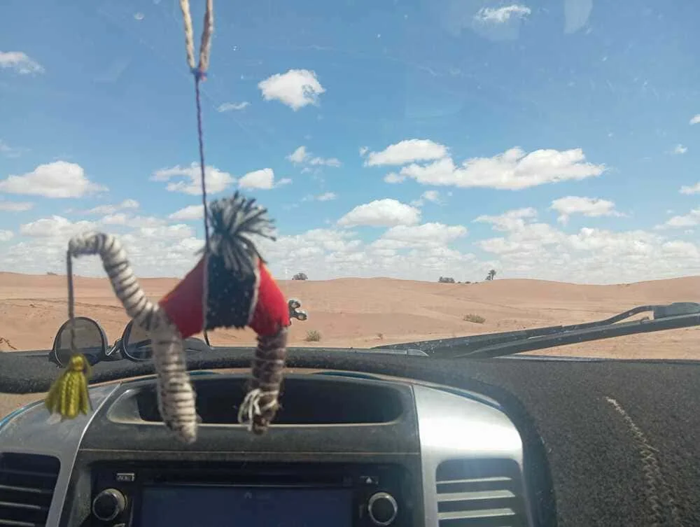 Interior view of a 4x4 during a 6-day journey in the Moroccan Sahara with ADN Sahara, showing a handmade Berber camel object and desert landscapes outside