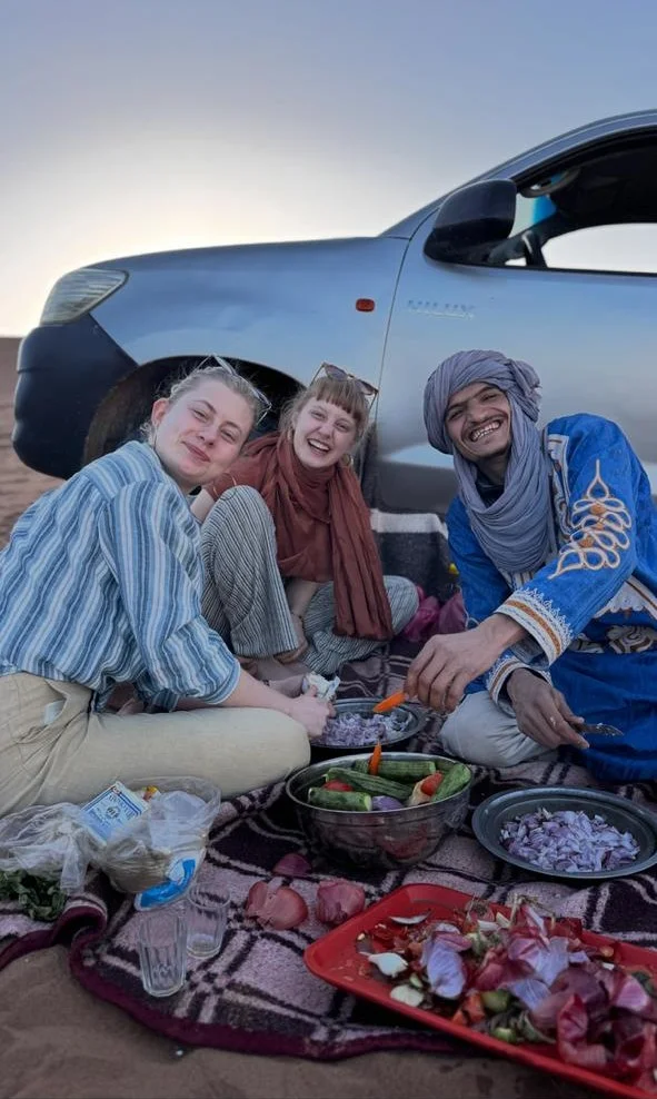 Guests preparing a traditional Moroccan tagine with a local guide during a desert lunch experience near M’Hamid