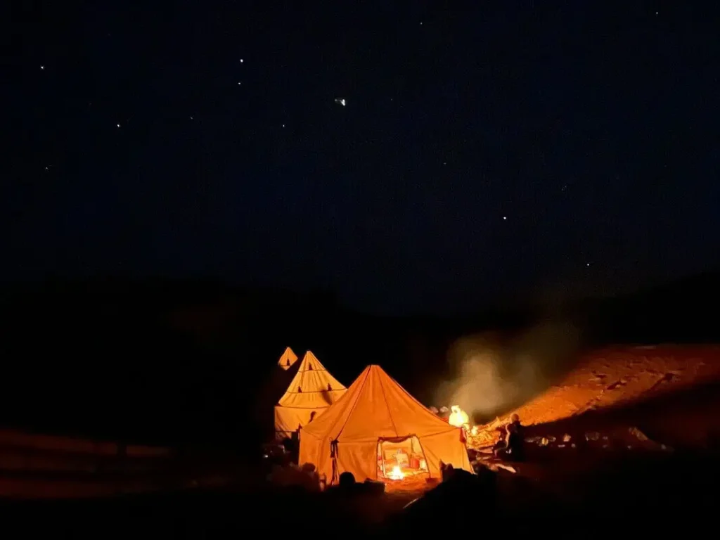 Camp nomade au Sahara marocain à M'Hamid, tentes éclairées à la nuit tombée au pied des dunes