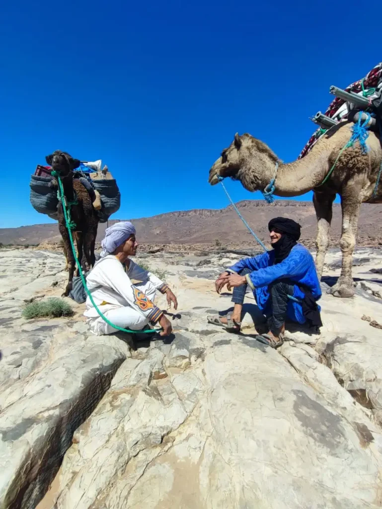 Lahsan et Moubarak assis dans le reg avec leurs dromadaires chargés pendant l’organisation d’un voyage privé sur mesure dans le désert du Maroc