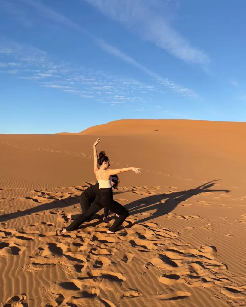 Yoga retreat in the Sahara with two women practising by the desert dunes