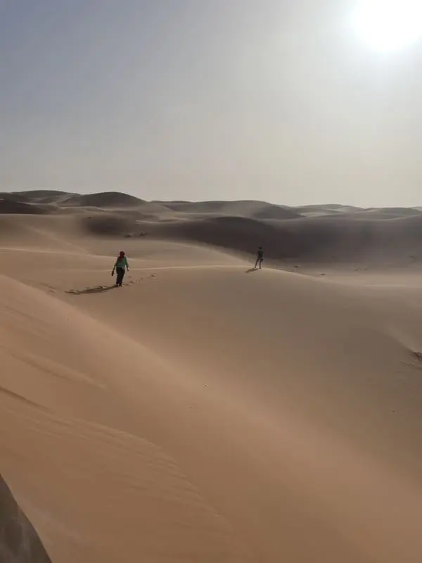 Deux voyageurs à pied traversent les dunes du Sahara marocain vers l’Erg Zahar à l’heure du coucher du soleil