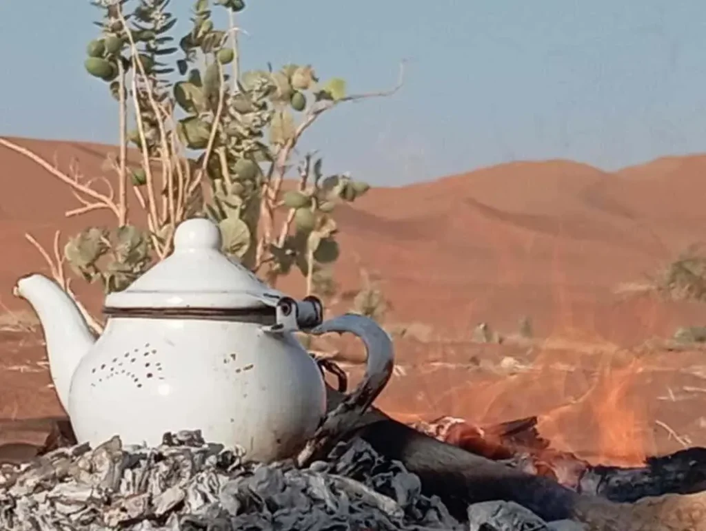 Théière sur les braises au cœur du Sahara marocain, avec les dunes de l’Erg Chegaga à l’horizon
